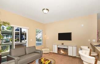 A living room with a grey couch, a coffee table with fruit on it, a fireplace, and a television at The Landing Apartments and Townhomes, Oregon, 97045