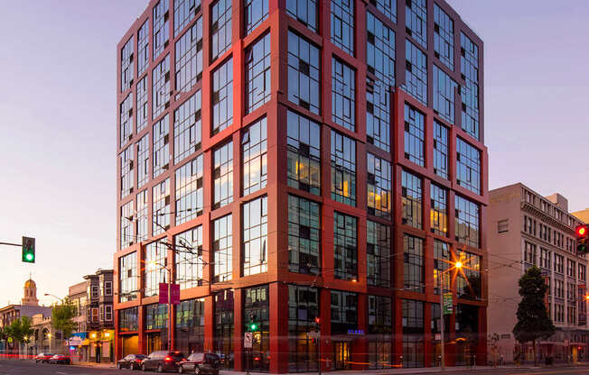 A tall red building with many windows stands in the middle of a street.