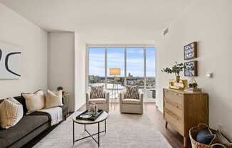 A living room with a grey couch, a coffee table, and a large window with a view of the city.