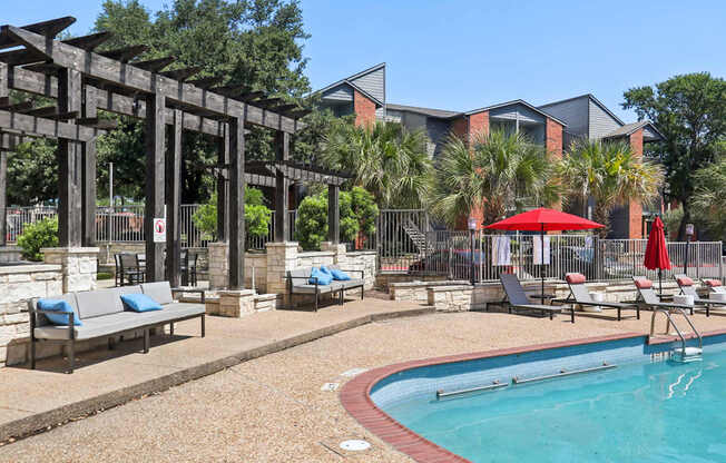 A pool area with a red umbrella and a bench.