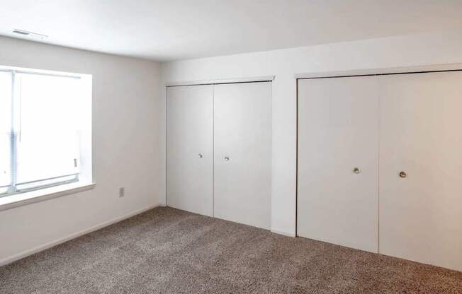 a bedroom with carpet and white walls and closets