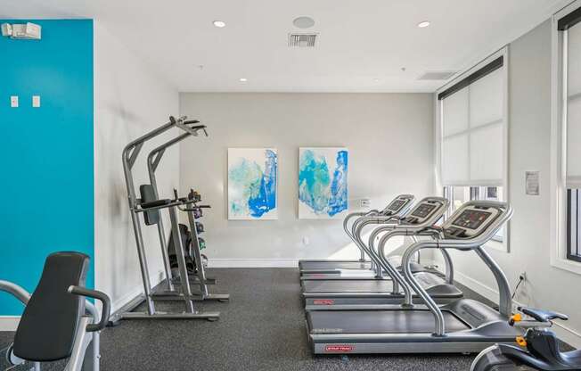A gym with treadmills, a stationary bike, and a painting on the wall.