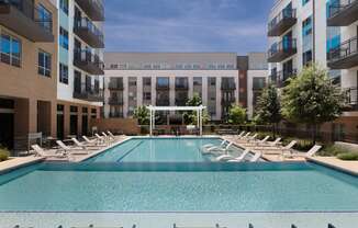 a swimming pool with chaise lounge chairs in front of an apartment building