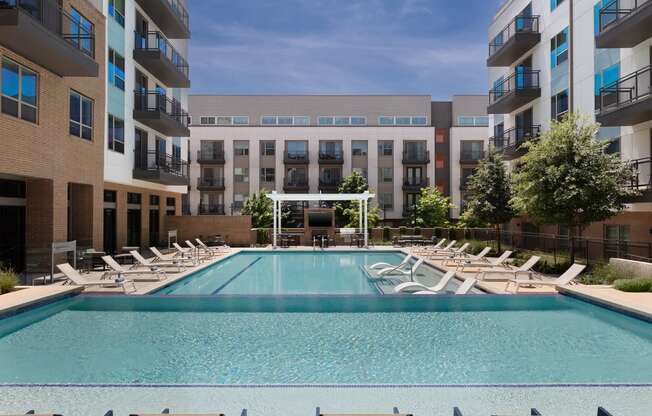 a swimming pool with chaise lounge chairs in front of an apartment building