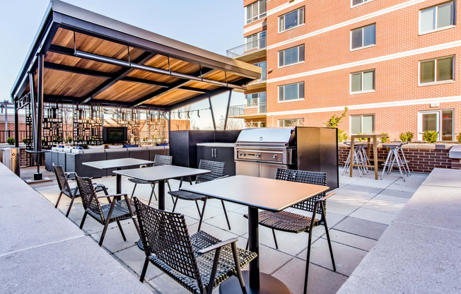 a patio with tables and chairs and a barbecue grill