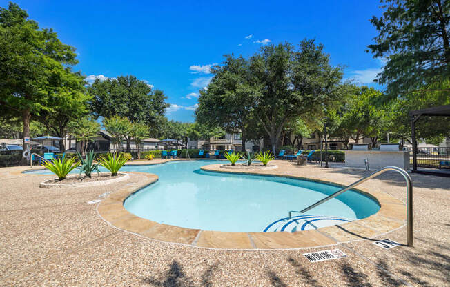 A large outdoor swimming pool surrounded by trees and plants.