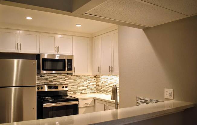 Kitchen with stainless appliances, white cabinets, and tiled backsplash