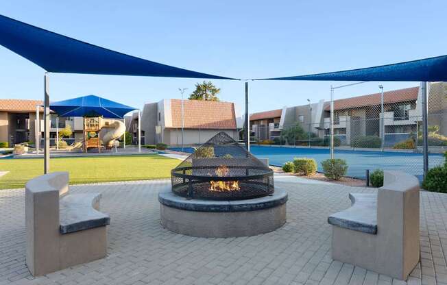 A fire pit is surrounded by two concrete benches under a blue canopy at Denim Scottsdale, Scottsdale, AZ