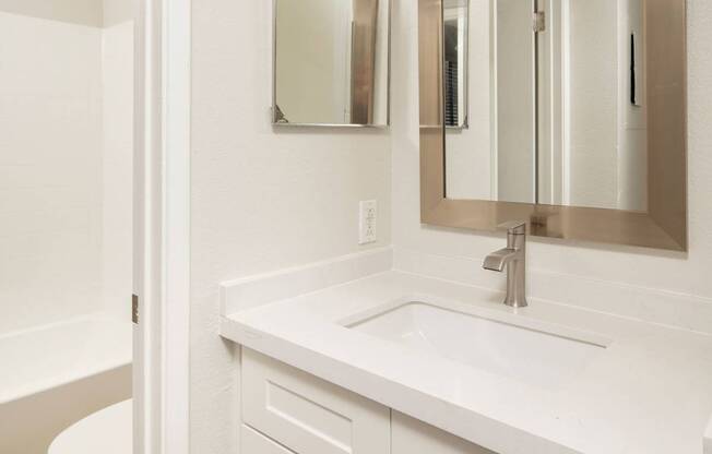 A white bathroom with a sink, mirror, and toilet.