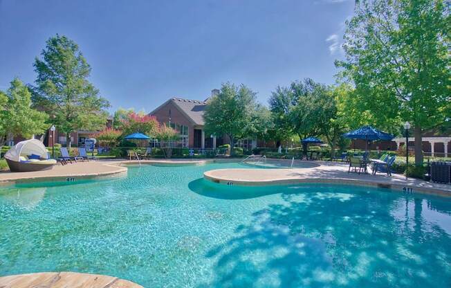 A large swimming pool surrounded by trees and umbrellas.
