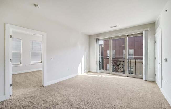 A room with a carpeted floor and a sliding glass door leading to a balcony.