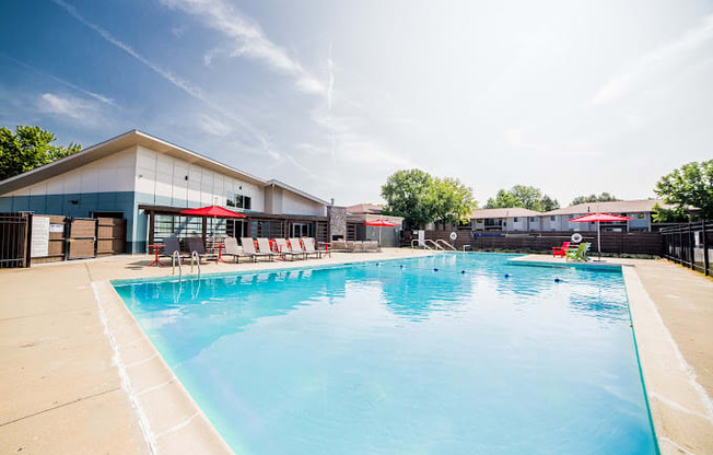 a large swimming pool with lounge chairs and umbrellas in front of a building
