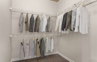 a walk in closet with white walls and a white rod with clothes hanging on it