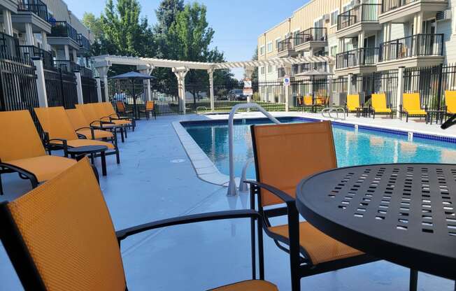 a poolside patio with chairs and tables at an apartment building