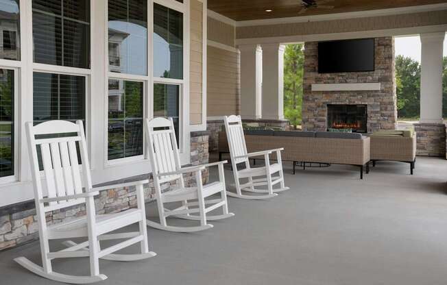 A row of white rocking chairs are lined up in front of a fireplace.