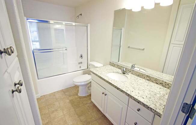 A bathroom with a toilet, sink, and mirror at The Kitt at Warner Center Apartments, California, 91303
