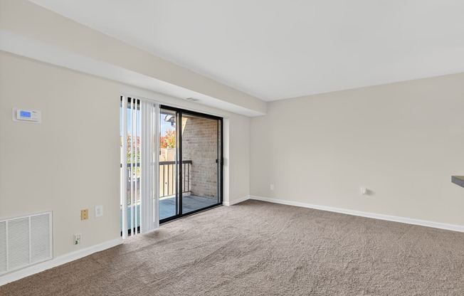 A room with a carpeted floor and a sliding glass door leading to a balcony.
