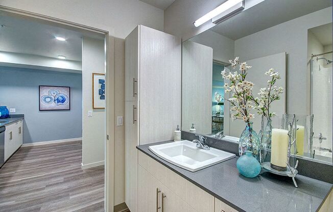 A bathroom with a sink, mirror, and a vase of flowers. at Ravello Apartments, Redmond, WA