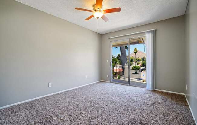 an empty living room with a ceiling fan and a door to a patio