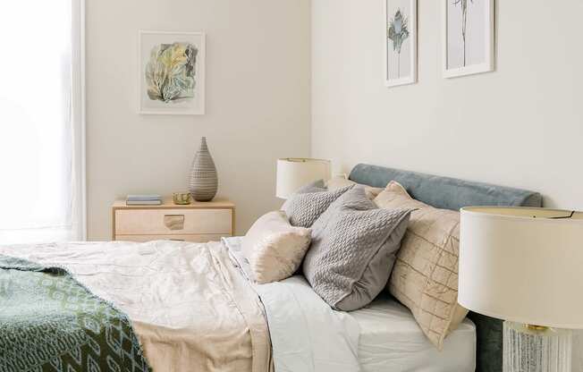 A bedroom with a bed, nightstand, lamp, and two framed pictures on the wall at The Pennsylvanian Apartments, Pittsburgh, PA