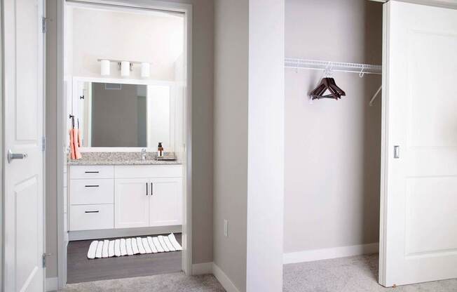 Modern apartment bathroom featuring stain-resistant floors and elegant granite countertops. The adjacent spare bedroom boasts plush carpeting and a spacious closet with sliding doors