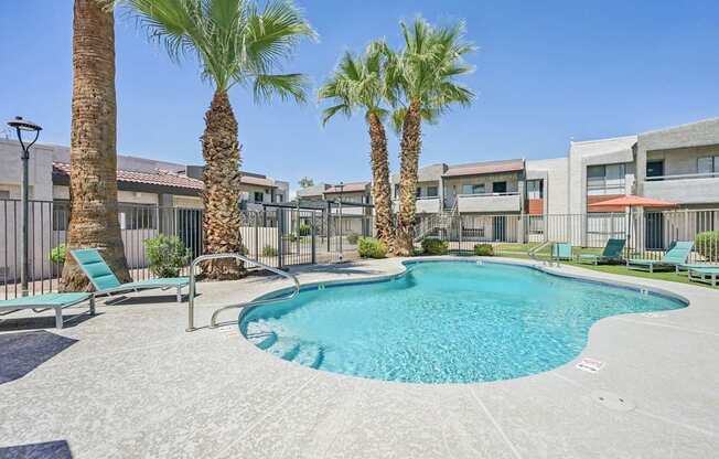 A pool surrounded by palm trees and lounge chairs.