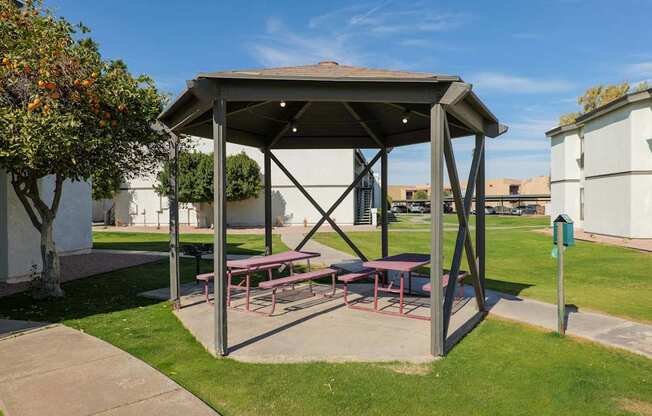 A picnic shelter with a table and benches is situated in a grassy area.