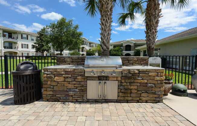 A stone fireplace with a grill on top is in the middle of a brick patio.