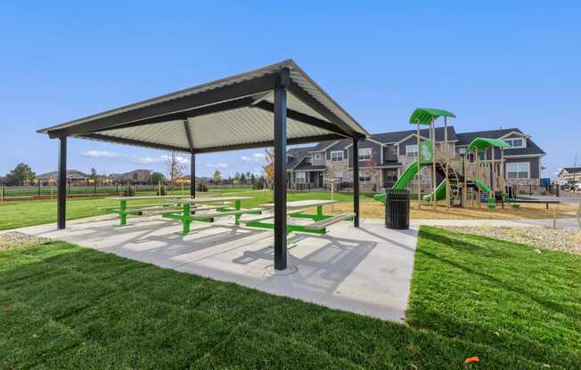 a picnic pavilion with benches and a playground in a park