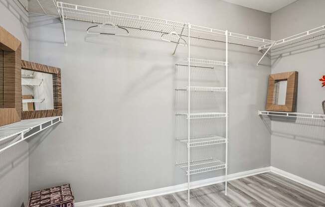 A walk-in closet with white shelving and a mirror on the wall.