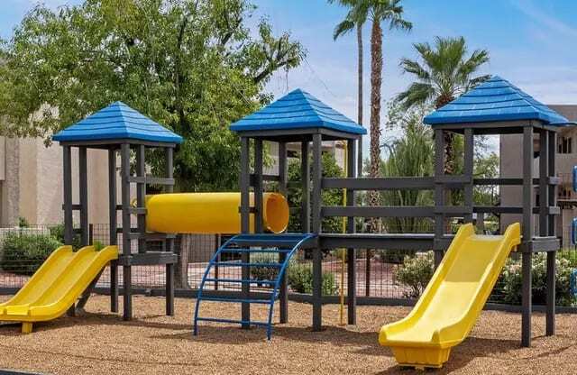 A playground with a yellow slide and blue roofed structures.