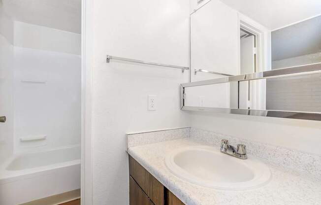 A white bathroom with a sink, mirror, and bathtub.