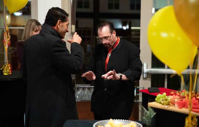 two men talking at a party with yellow balloons