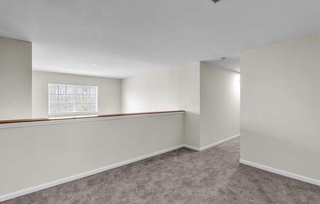 Upstairs room with a carpeted floor and a window in the Ledges Apartments.