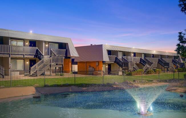 A fountain in the middle of a pool in front of a building.