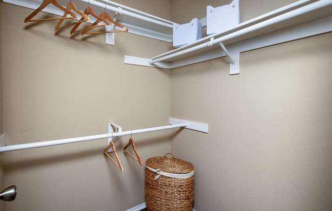 A white metal rod is mounted on a wall with clothes hangers and a basket underneath.