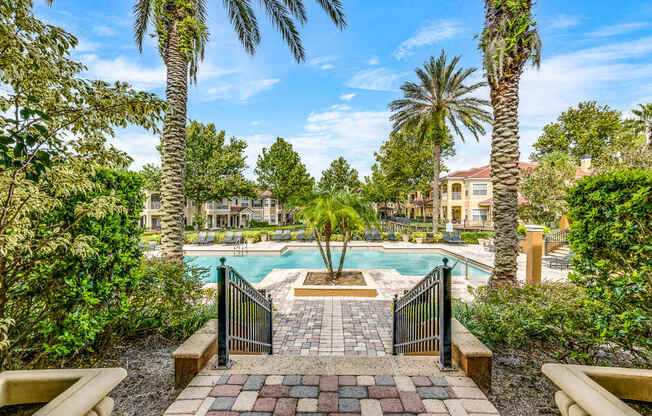 A pool surrounded by palm trees and a brick walkway.