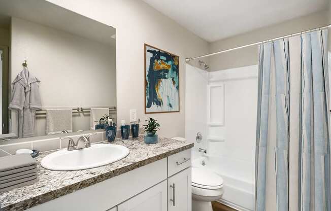 Full bathroom with vanity sink, under sink cabinets, large mirror, toilet, bathtub, and shower. Staged with plants, a shower curtain, and towels.at Wildflower, Kennewick, WA 99336