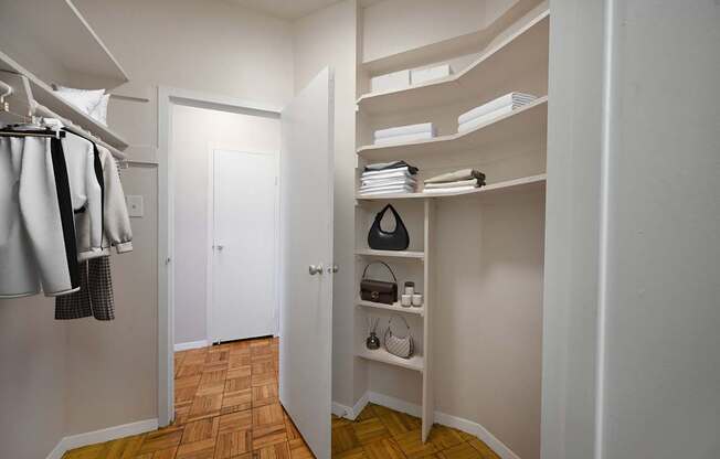 A hallway with a white door and a white closet with a shelf and a black speaker.