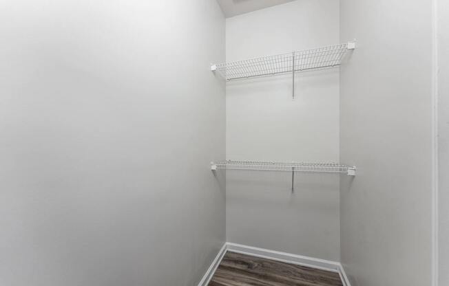 A white closet with a wooden floor and two shelves.