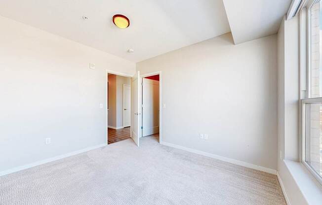 A large, empty room with a carpeted floor and a window on the right side.