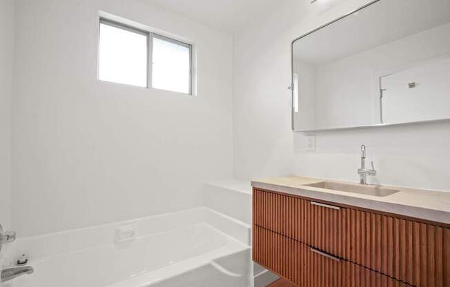 A white bathroom with a wooden vanity and a bathtub.