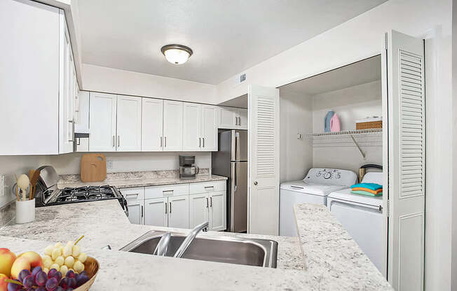 A kitchen with a breakfast bar, white cabinets and a washer/dryer at West Hampton Park Apartments in Elkhorn, NE 68022