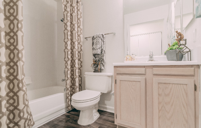 Model bathroom at our apartments in Antioch, featuring wood grain floor paneling and a shower / bath combination.