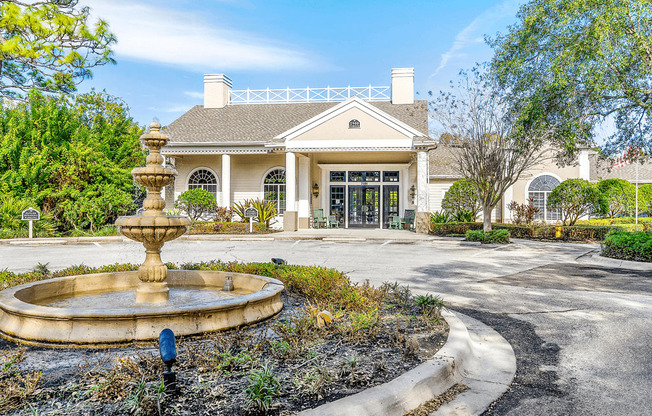 Exterior of clubhouse and leasing office with parking lot, a water fountain feature in the foreground surrounded by native landscape