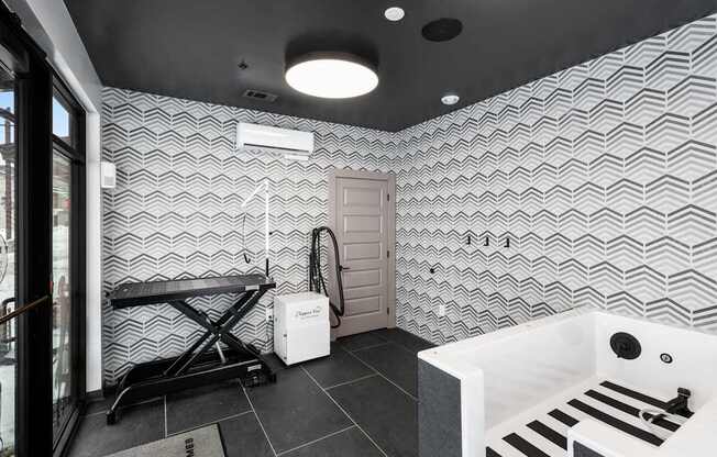 A bathroom with a white tub and a black and white tiled wall.