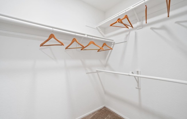 a walk in closet with white walls and orange hooks