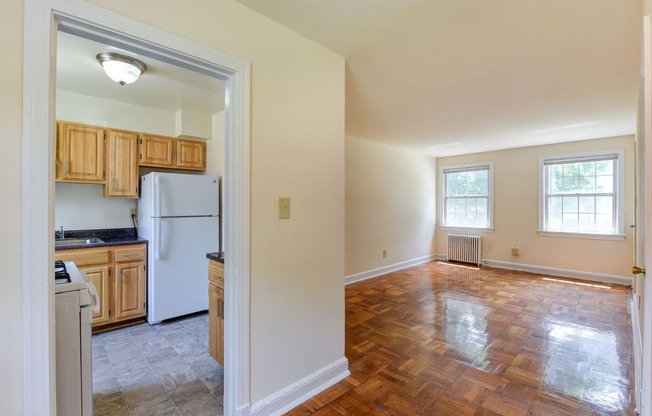 vacant living area with hardwood flooring, large windows and view of kitchen at colonnade apartments in washington dc