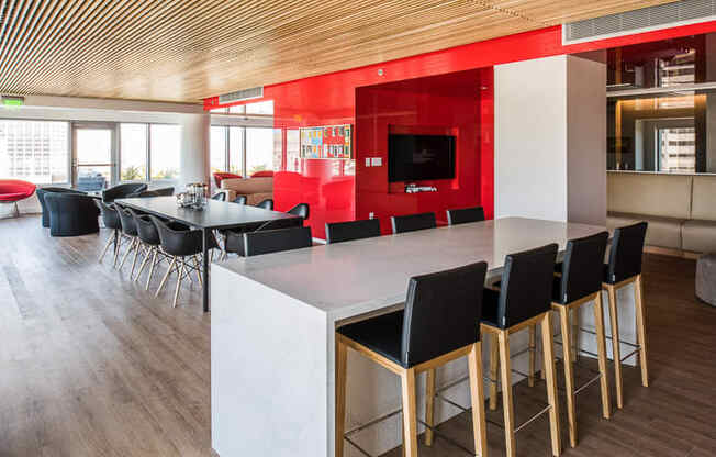 a communal area with a large table and chairs and a red wall with a television in the