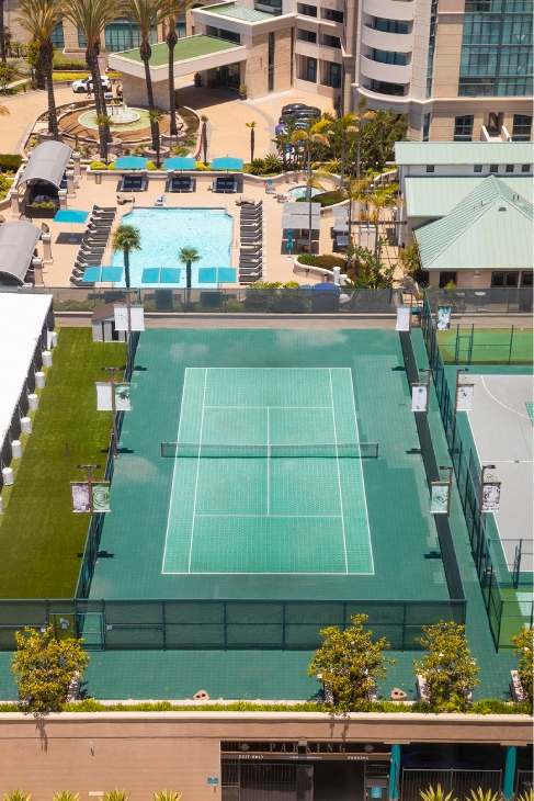 Tennis court surrounded by palm trees and buildings. at Towers at Costa Verde Apartments, San Diego, CA